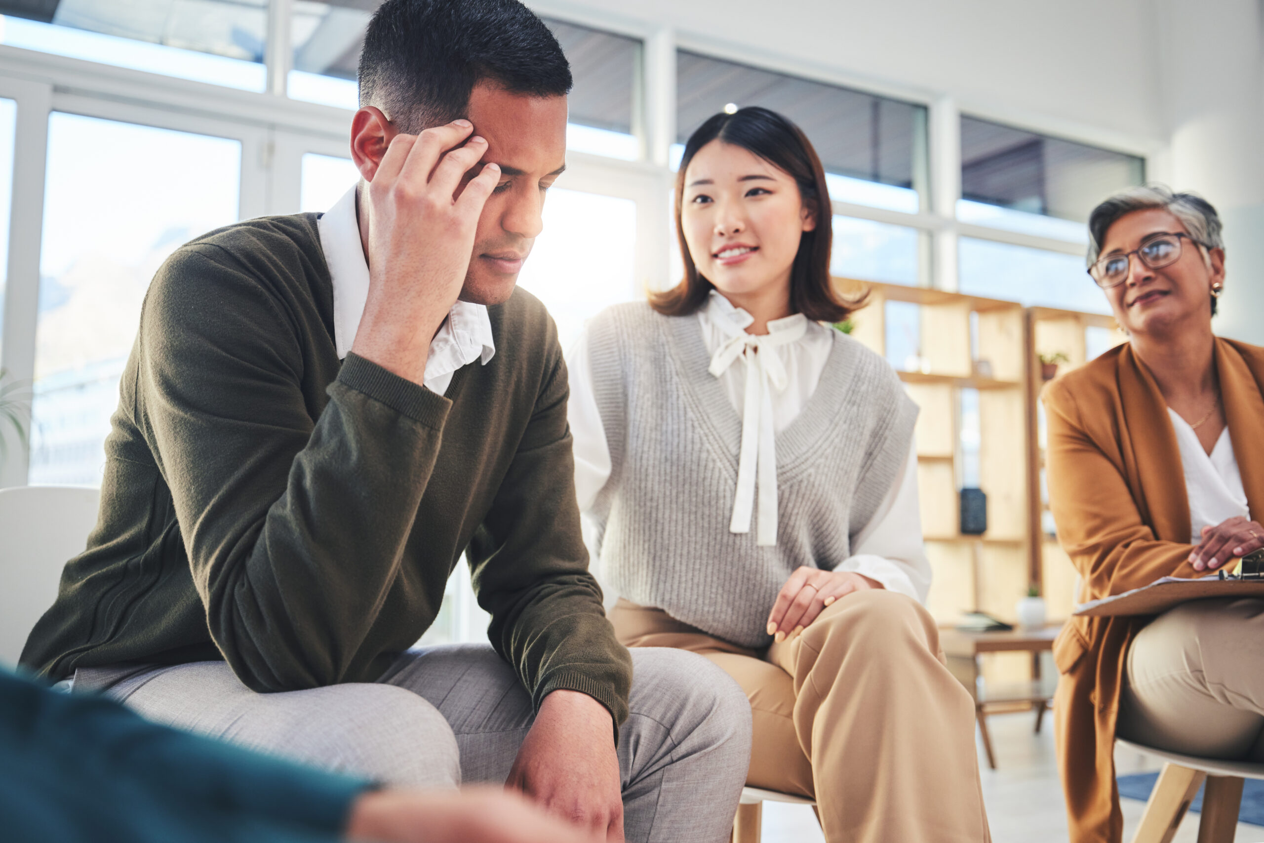 Man experiencing stress during group therapy session, supported by therapist and peers.