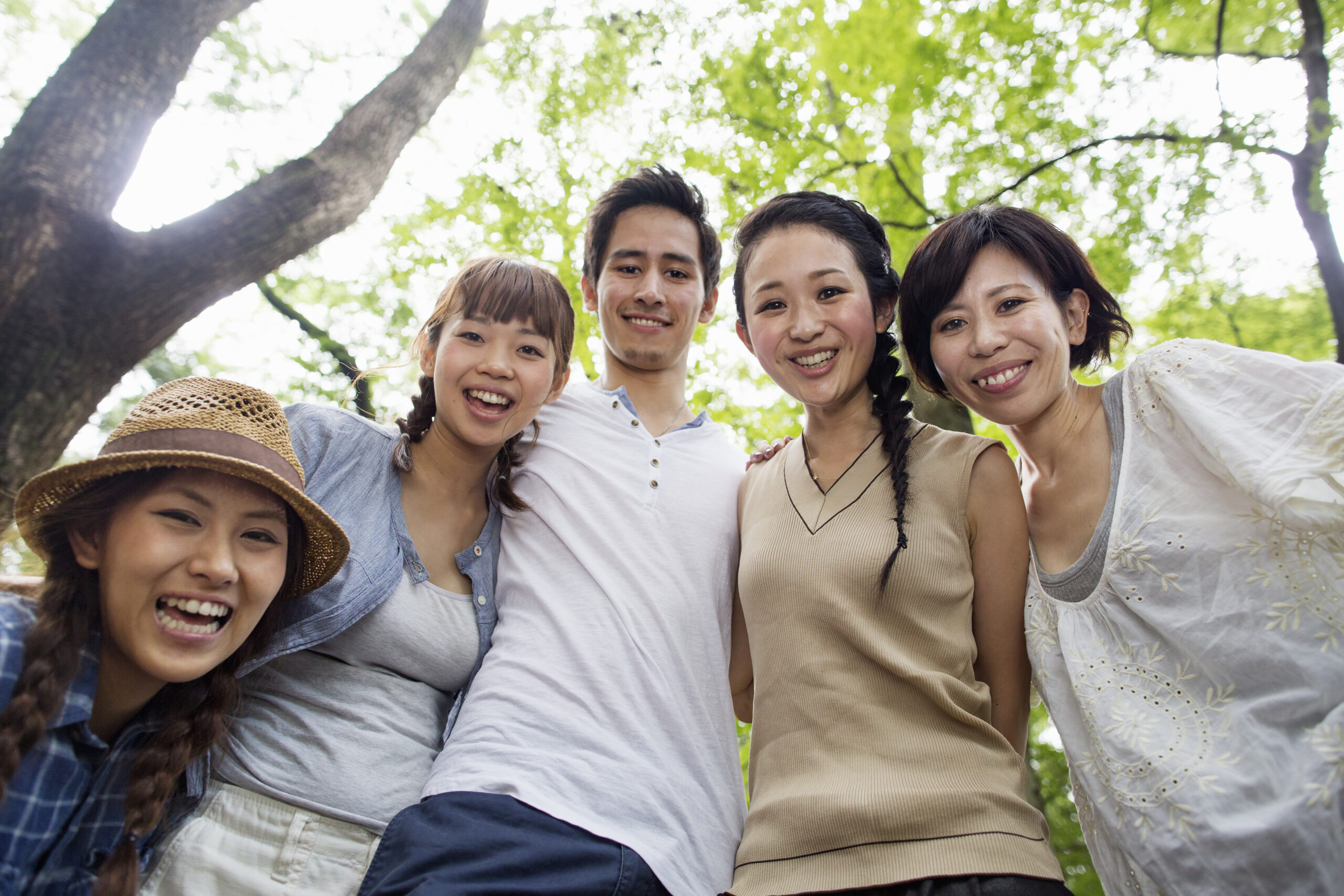 Five smiling friends embrace outdoors, enjoying nature.
