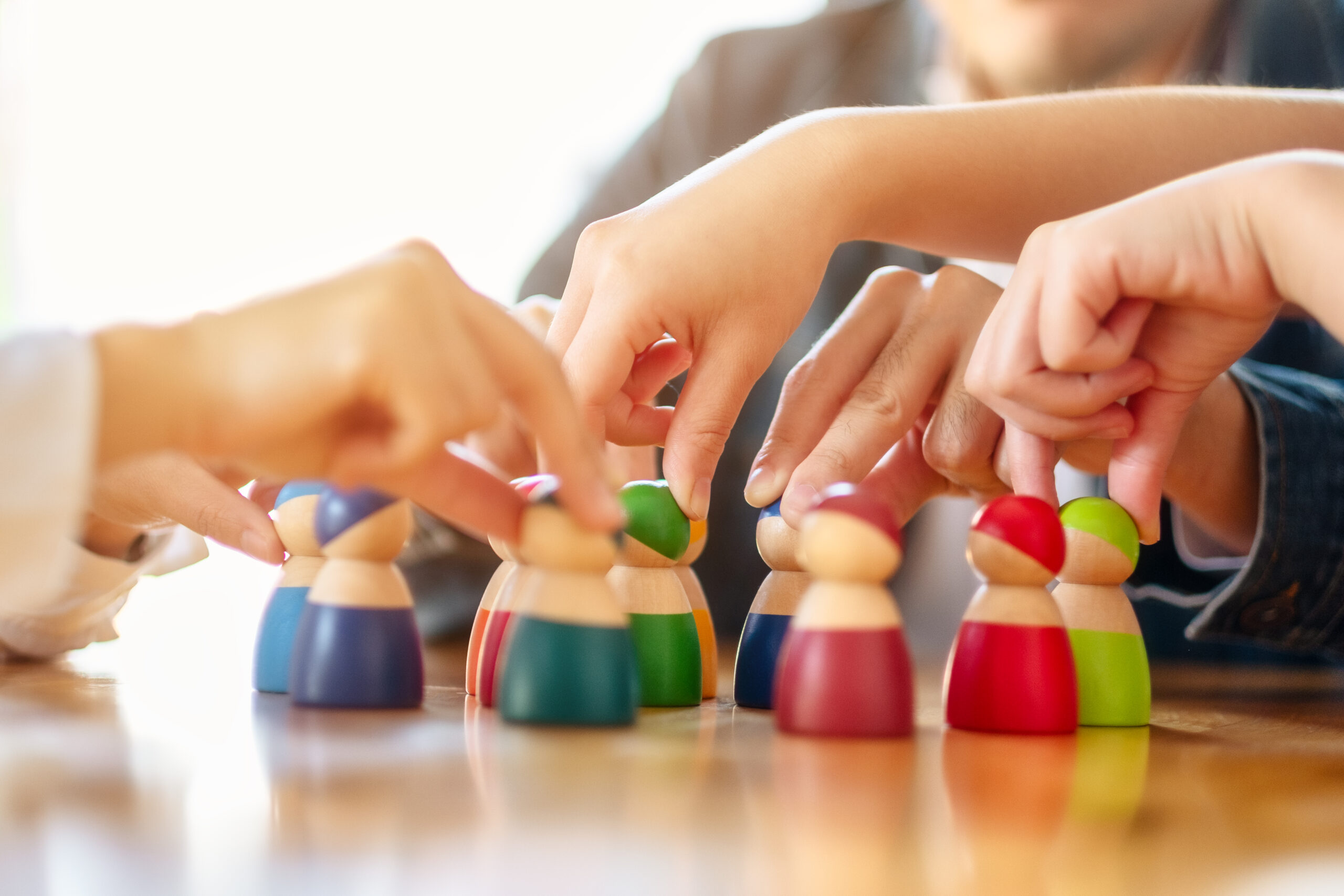 Hands arranging colorful wooden people figures; teamwork and collaboration concept.
