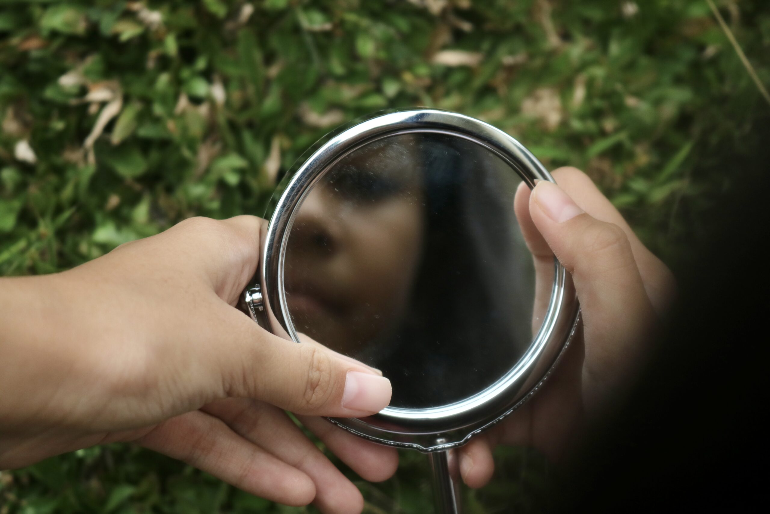 Person holding a hand mirror, reflecting their face.