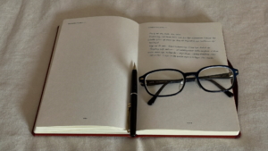Open notebook, pen and reading glasses on ivory linen