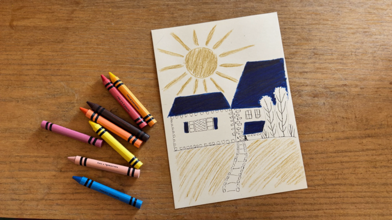 Crayons beside a child's drawing of a sun