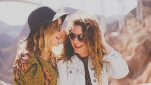 Two happy women whispering secrets, enjoying a sunny day.