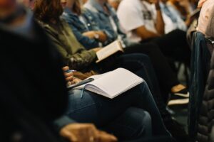 People taking notes at a conference, focusing on a notebook and pen.